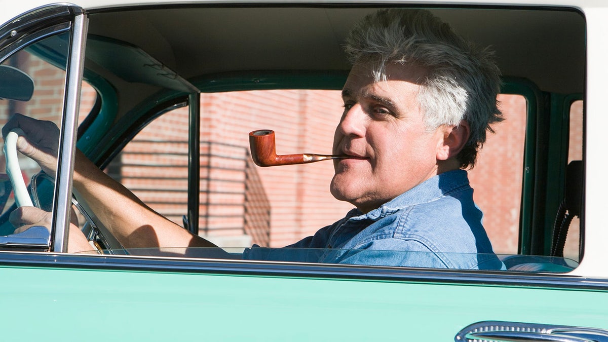 Close-up of Jay Leno sitting in a car and smoking a pipe