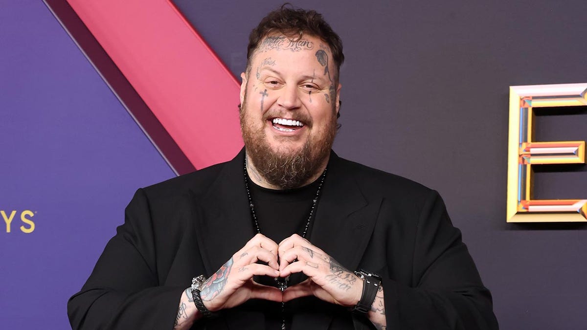 Jelly Roll in a black suit forms a heart with his hands at the Emmy Awards