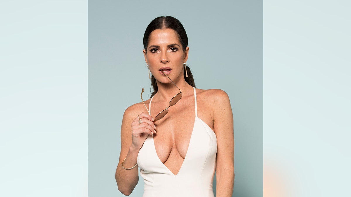 Kelly Monaco in a deep white outfit seductively holds her sunglasses in her hand