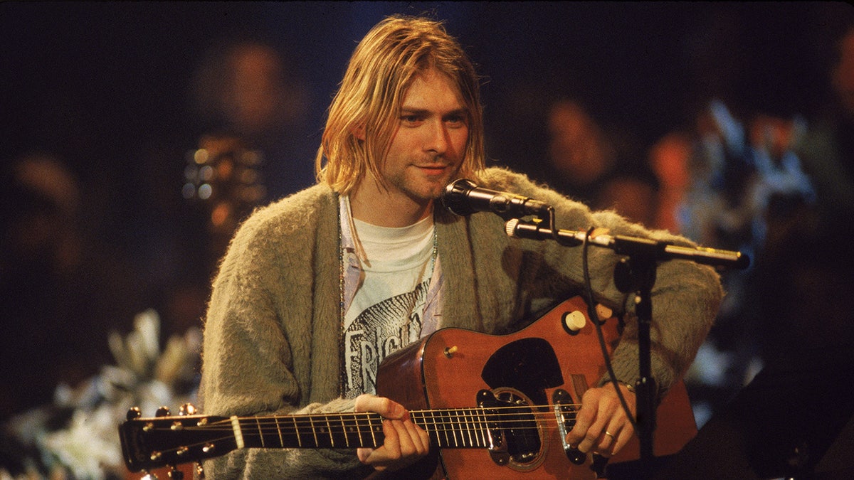 Kurt Cobain sitting connected  signifier    successful  beforehand   of a microphone with a guitar