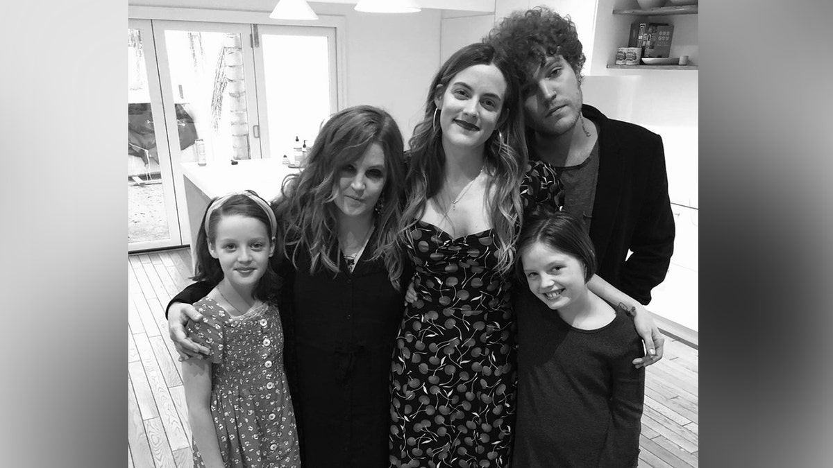 A black and white photo of Lisa Marie Presley embracing her four children, twins Harper Vivienne Ann Lockwood and Finley Aaron Love Lockwood on either side, and daughter Riley Keough and son Benjamin Keough