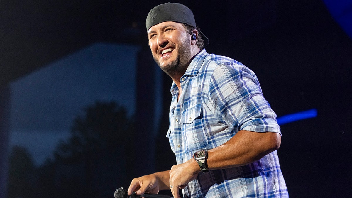 Luke Bryan smiles on stage with blue flannel