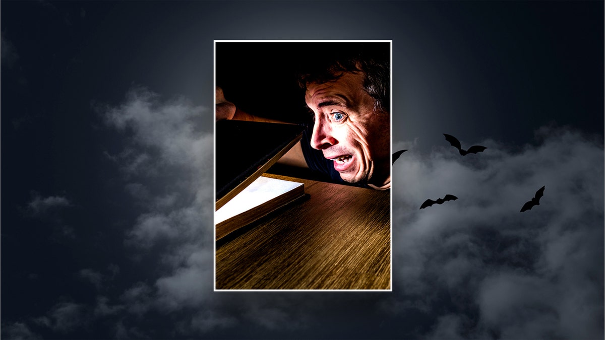 Man opening a scary book with a night sky in the background