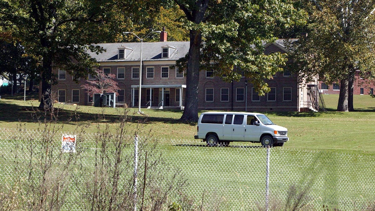 A white van is parked outside a West Virginia prison (Alderson Federal Prison Camp) with a green lawn and brick building where Martha Stewart is imprisoned 