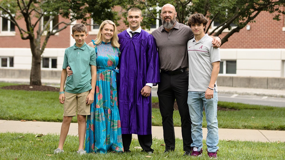 Melissa Joan Hart in a blue floral dress poses with her children, Tucker in a green shirt and khaki shorts, and son Mason in a purple graduation gown, husband Mark in a textured shirt and black pants and Brayden in a collared-shirt and jeans