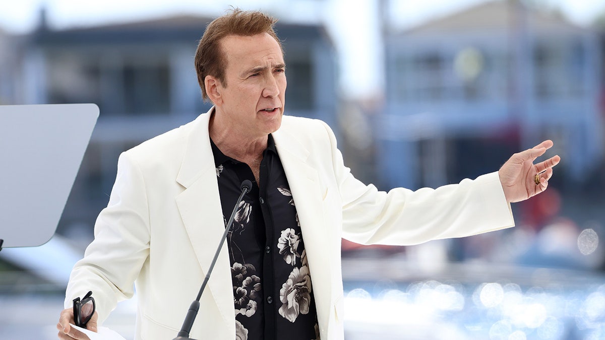 Nicolas Cage standing at a podium wearing a white coat.