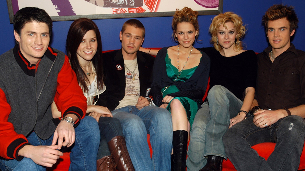 James Lafferty, Sophia Bush, Chad Michael Murray, Bethany Joy Lenz, Hilarie Burton and Tyler Hilton sit together on a red couch