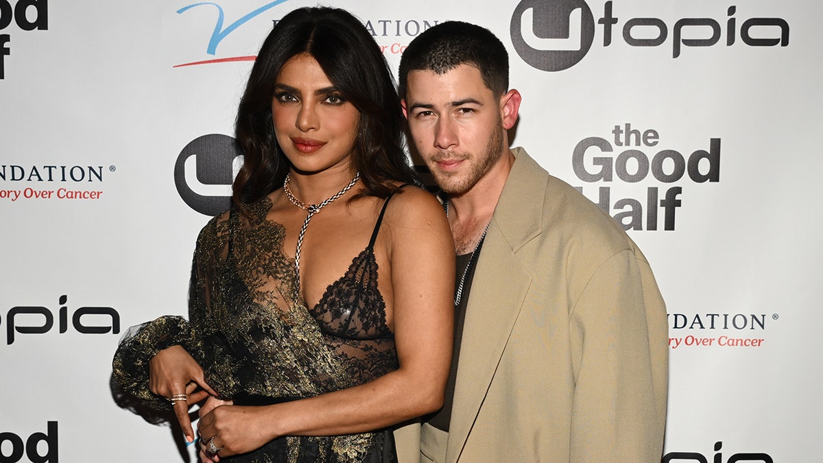 Priyanka Chopra in a lace bra and covering poses on the carpet with husband Nick Jonas in a tan jacket