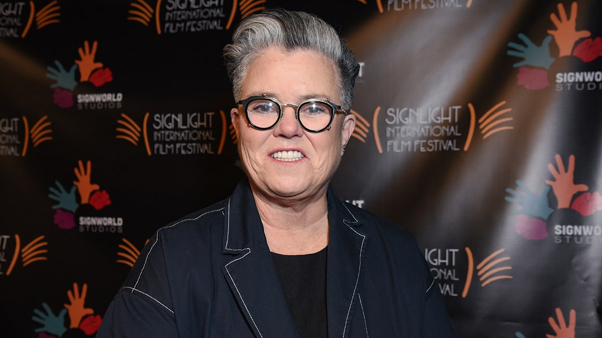 Rosie O'Donnell successful  a denim overgarment   smiles wearing circular achromatic  glasses connected  the carpet