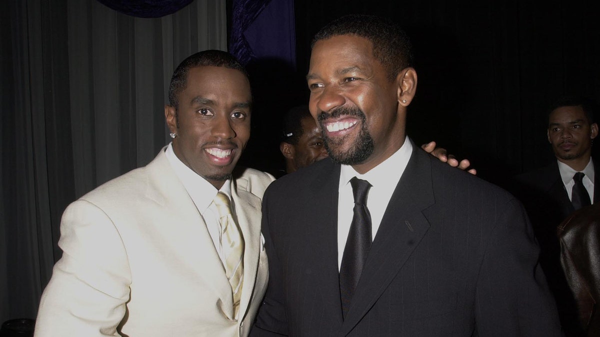 Sean Diddy Combs wears a achromatic  suit   and smiles adjacent  to Denzel Washington.