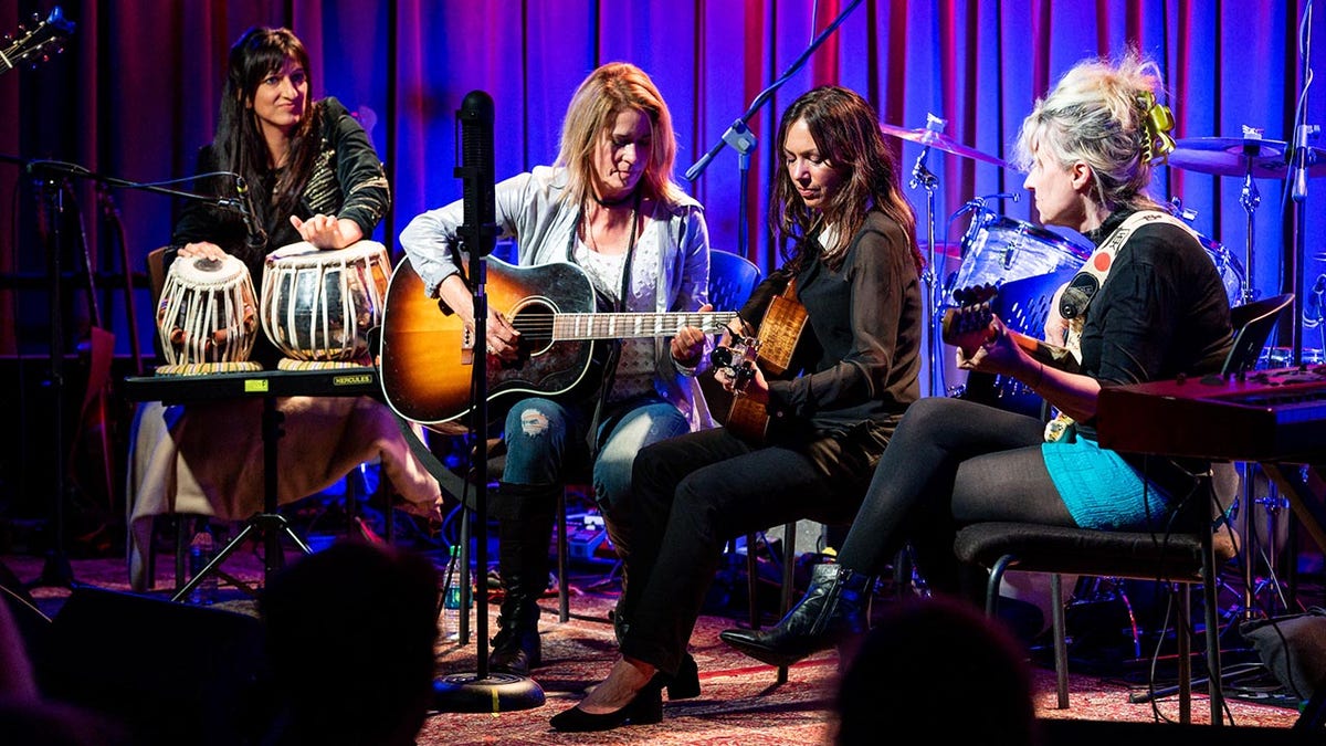 Meena Makhijani est assise sur scène avec Vicki Peterson et Susana Hoffs, membres des Bangles, toutes deux tenant des guitares et Annette Zalinskis tournée vers l'intérieur tenant également une guitare.