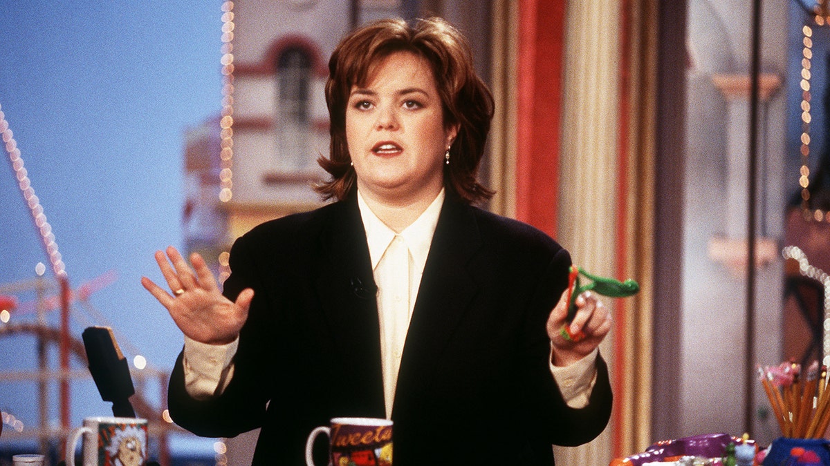 Rosie O'Donnell in a black suit puts her hands up as she hosts her talk show "The Rosie O'Donnell Show"