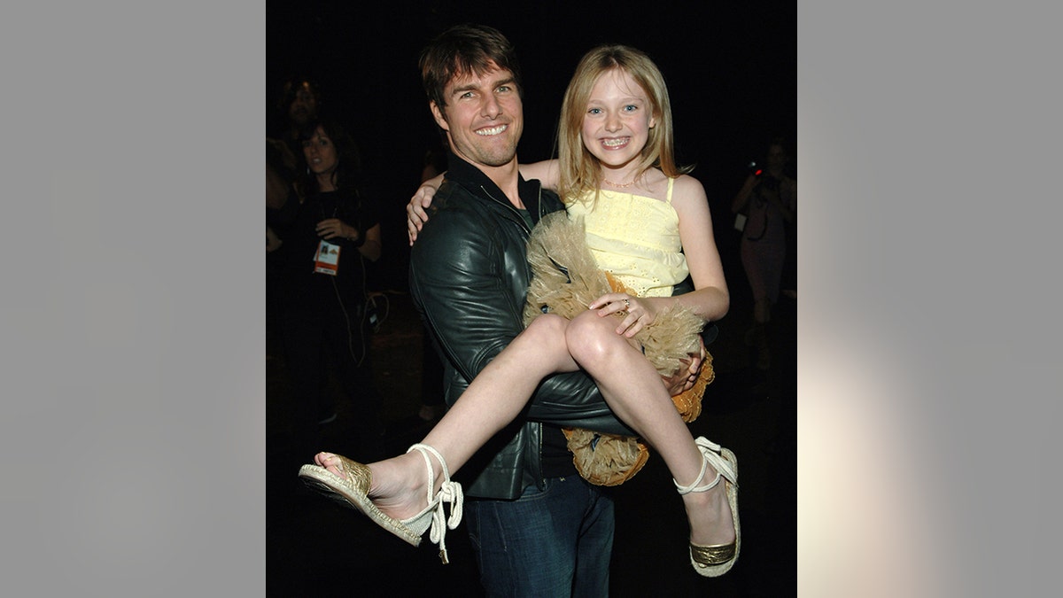 Tom Cruise con una chaqueta de cuero negra sostiene a una sonriente Dakota Fanning con un vestido amarillo en los MTV Movie Awards 2005