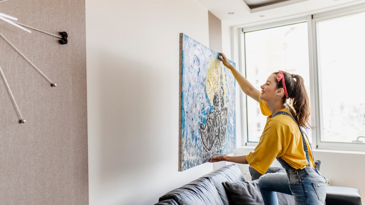 Una mujer cuelga arte mural en su casa.