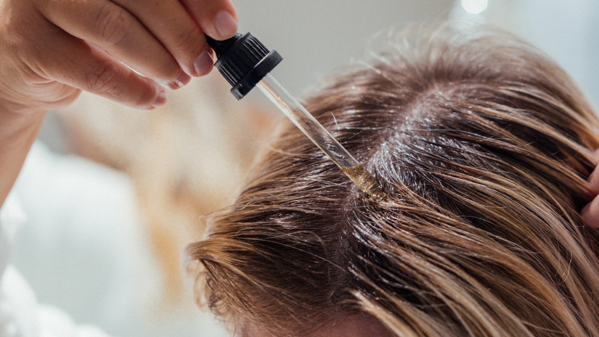 A woman applying oil to hair