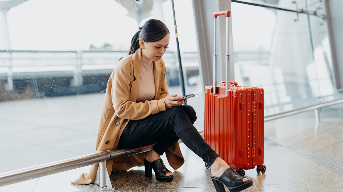 woman-unhappy-on-phone-at-airport-with-luggage