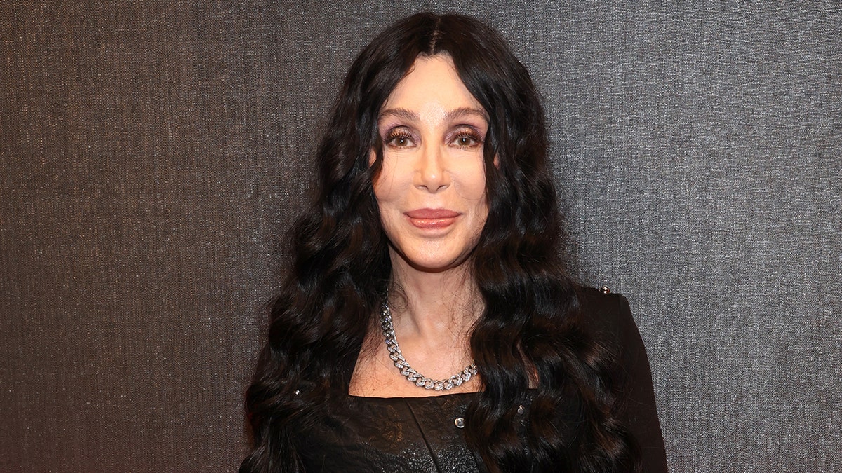 Cher with long curly black hair soft smiles on the carpet at the 2024 Rock & Roll Hall of Fame