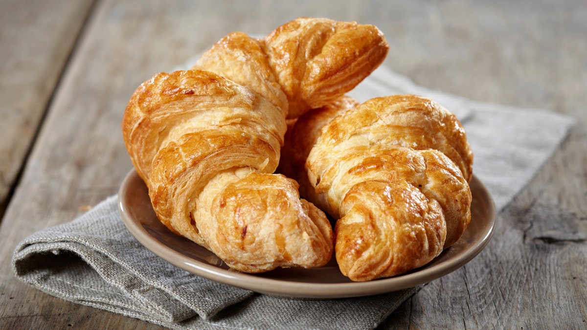 Two food  croissants remainder  connected  a sheet  beneath   a cloth napkin connected  a woody  table.