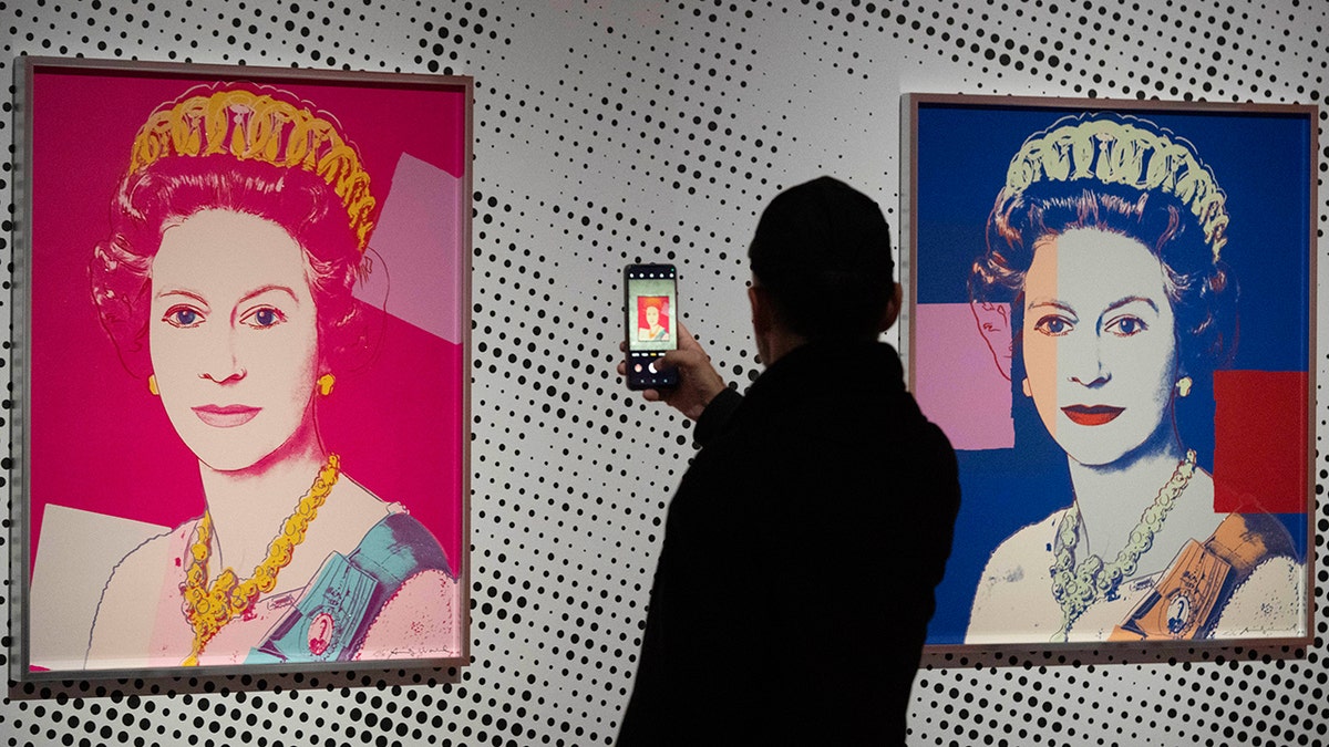 Un hombre toma una imagen de un retrato de Warhol que representa a la reina Isabel II