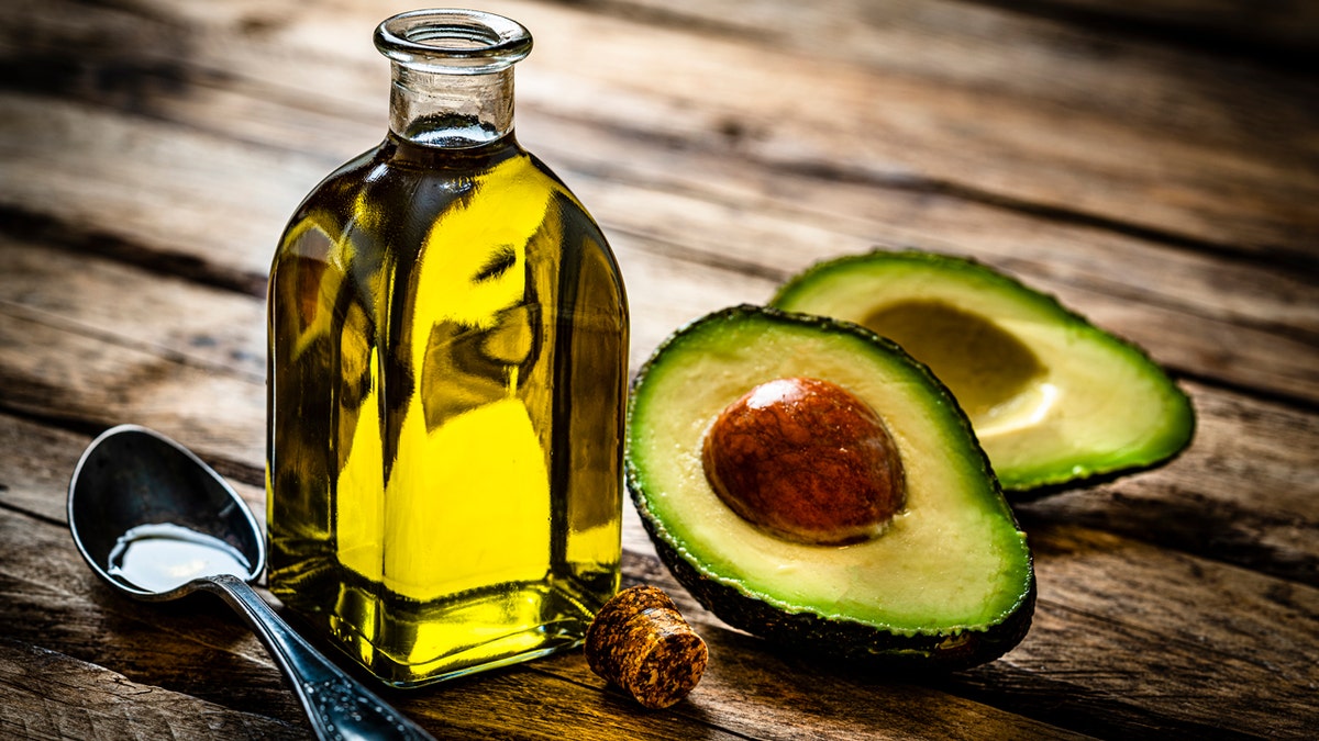 Avocado oil is shown next to an open avocado on a table.