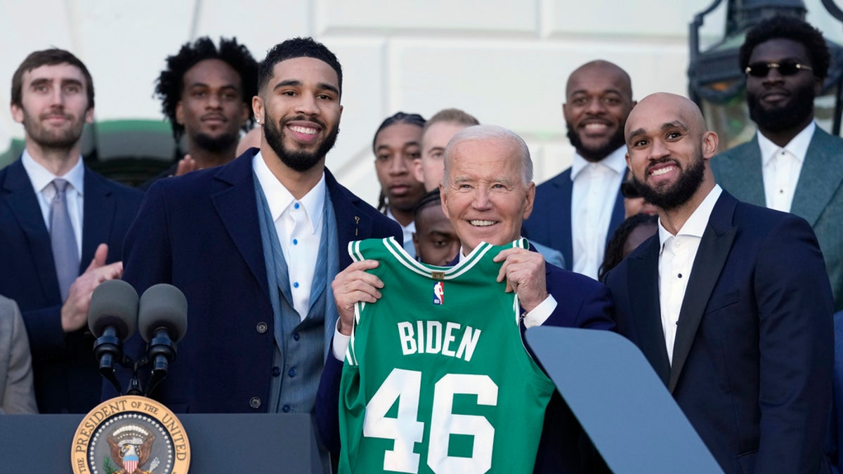 President Joe Biden, center, flanked by Boston Celtics players Jayson Tatum, left, and Derrick White, holds up a jersey they presented to him during an event to celebrate the team's victory in the 2024 NBA championship, on the South Lawn of the White House in Washington, D.C., Thursday.