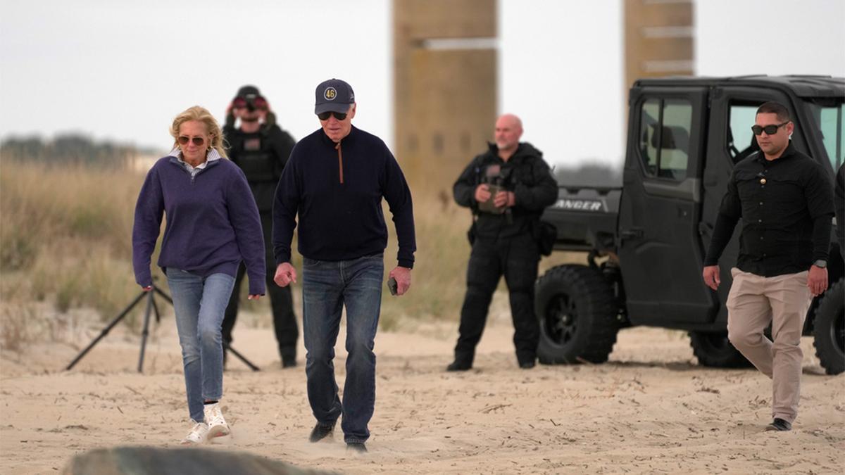 Biden and first lady walking on the beach as Secret Service agents look on