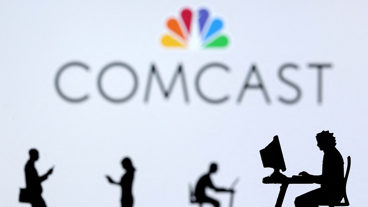 Illustration shows small toy figures with laptops and smartphones in front of displayed Comcast logo