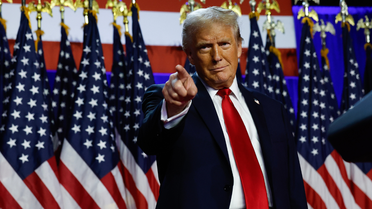 Trump gestures to supporters while standing in front of a row of American flags