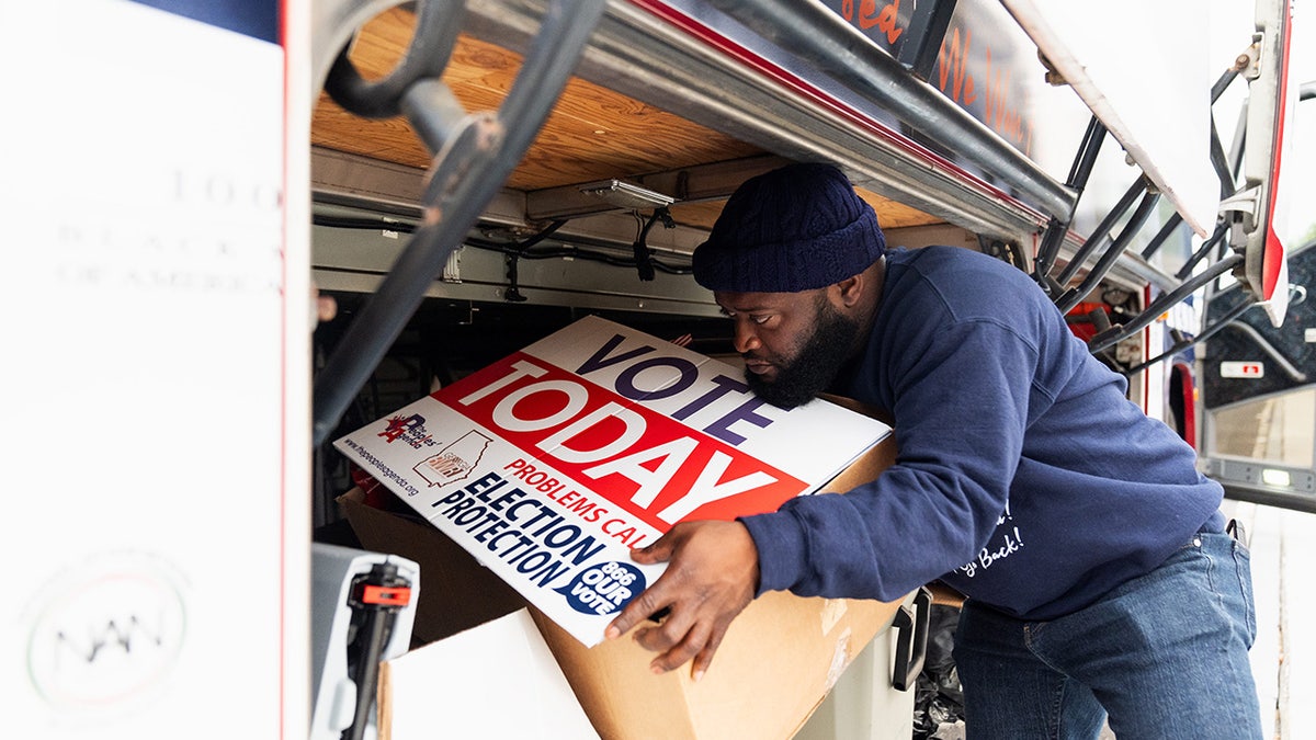 Sean Floyd, de la Coalición Nacional para la Participación Cívica de los Negros, ayuda a cargar carteles en un autobús antes de que él y otros encuestadores se dirijan al condado de Clayton para encuestar.