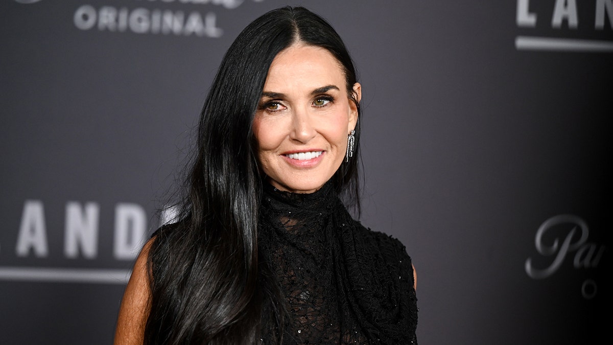 Demi Moore con un jersey negro de cuello alto sin mangas mira ligeramente a su derecha en la alfombra