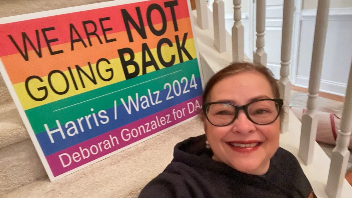 Deborah Gonzalez poses adjacent  to a rainbow-colored Harris-Walz sign