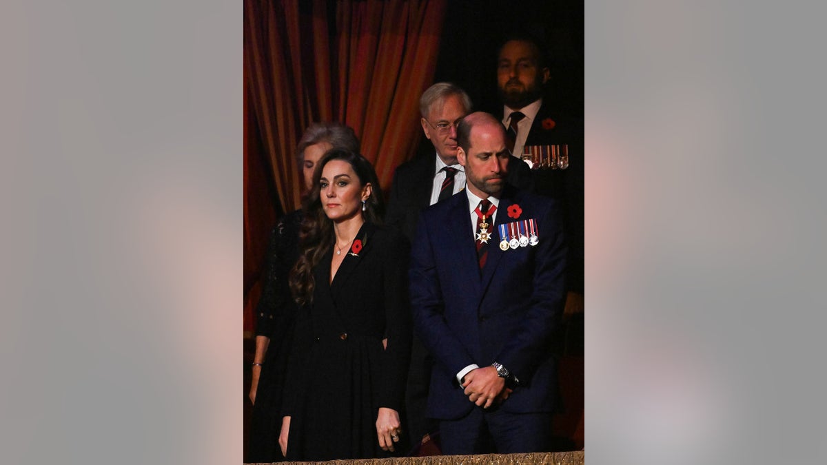 Kate Middleton standing next to Prince William who looks somber in a suit with medals at Royal Albert Hall