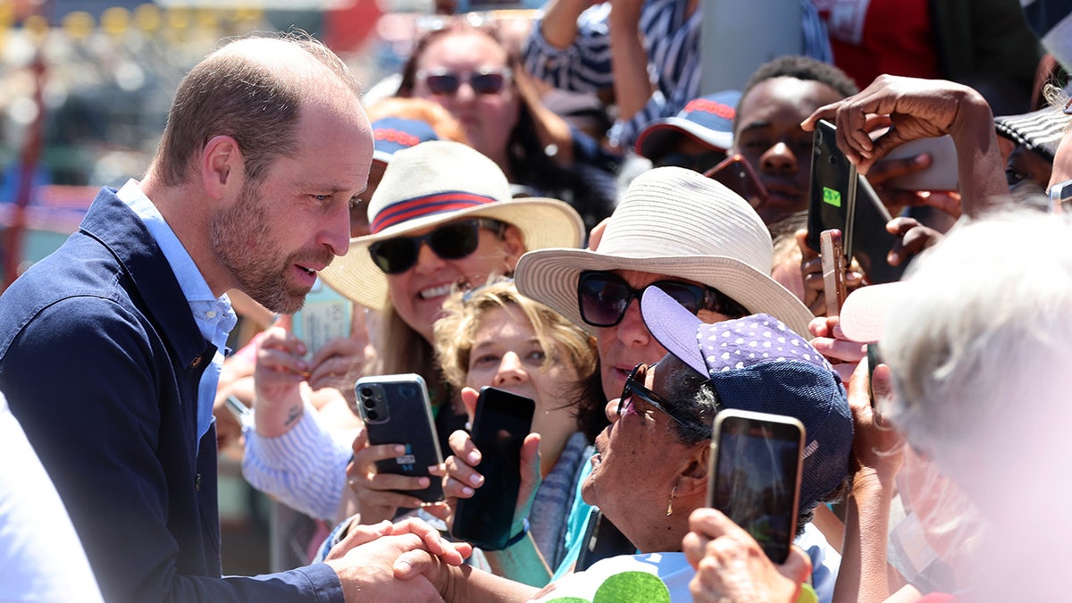 Prince William chatting to a crowd as some people hold onto their cell phones.