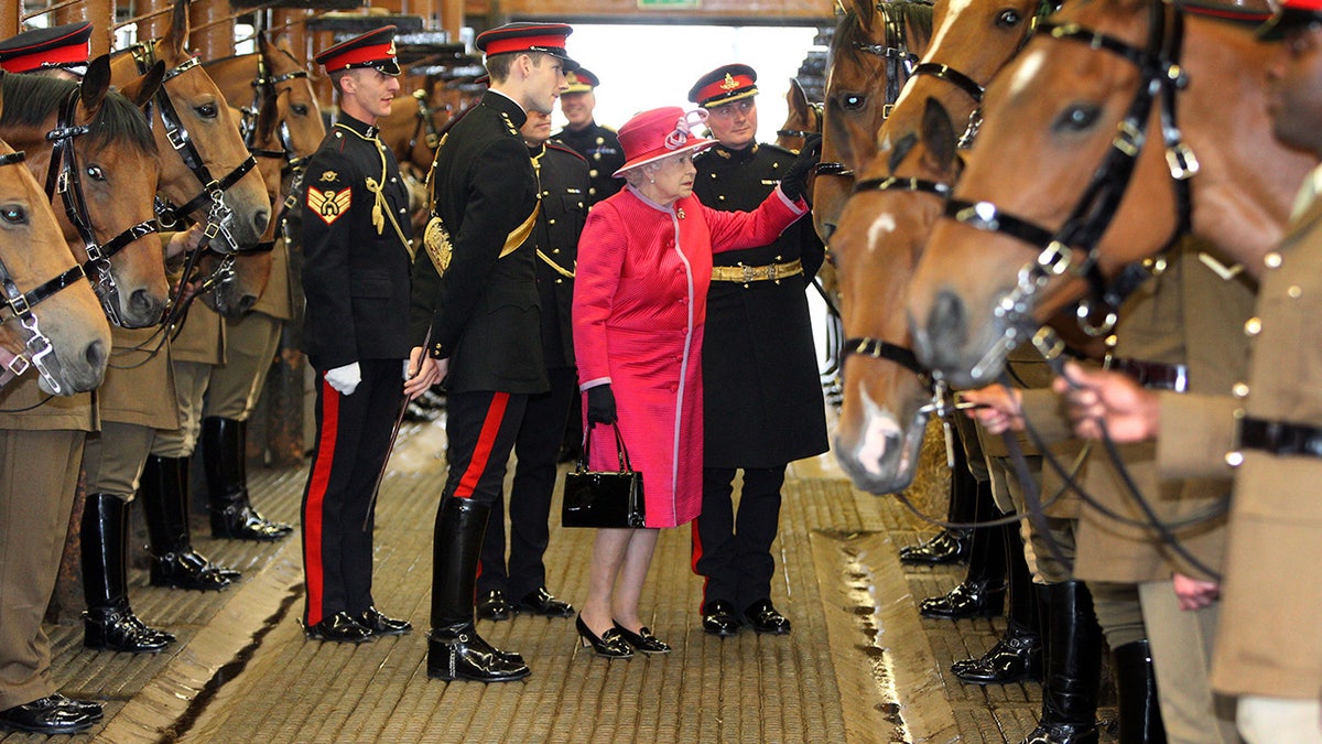 Queen Elizabeth wearing a hot pink coat surrounded by guards and brown horses.