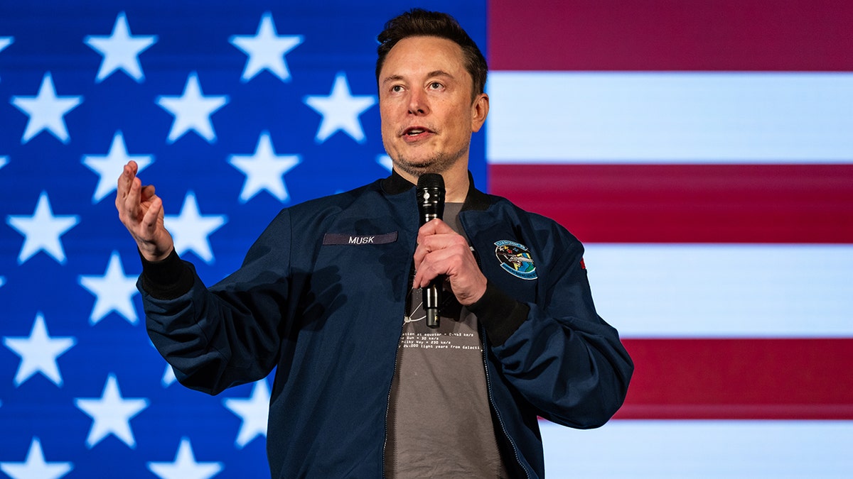 Elon Musk speaking in front of an American flag