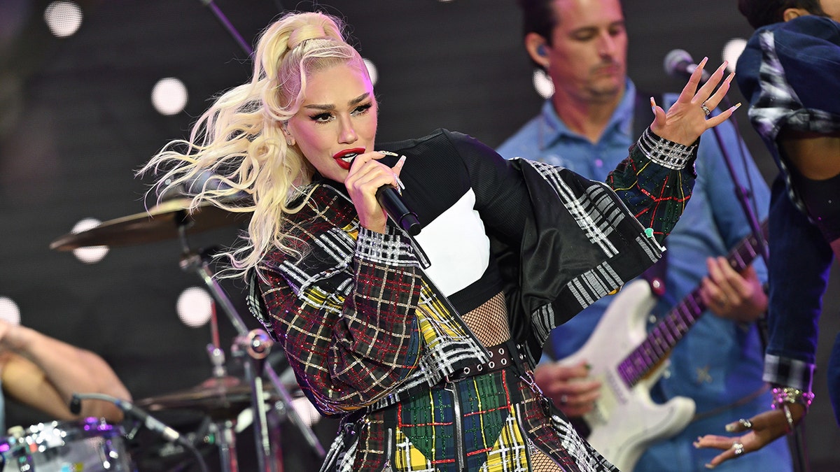 Gwen Stefani in a multicolored plaid jacket performs on stage