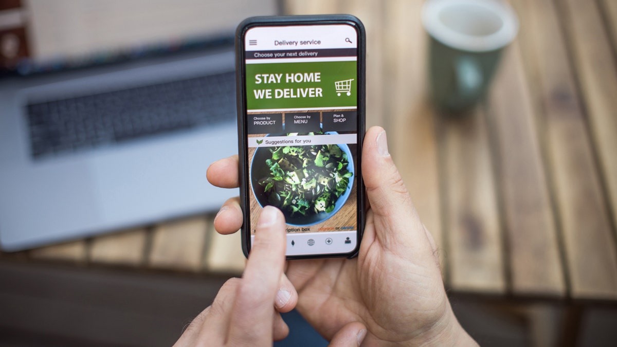 Hands prepare to place an order from a food delivery app on a cellphone.