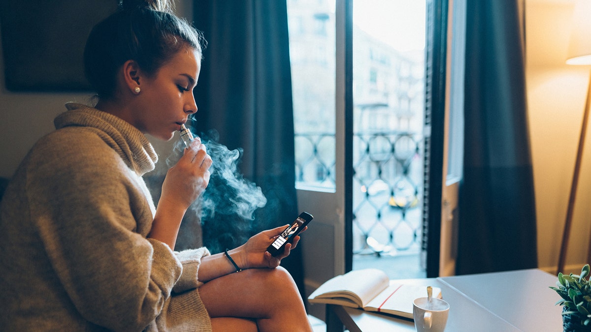 ragazza a casa che fuma sigarette elettroniche al telefono