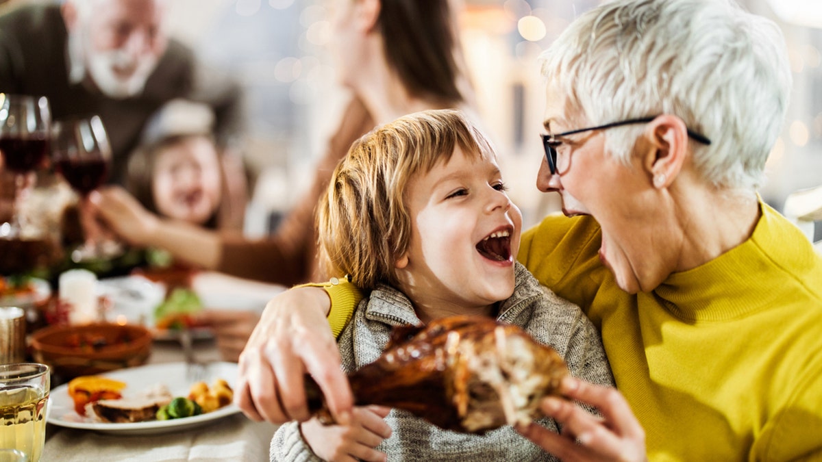 Happy boy and his grandmother having fun while about to eat turkey leg