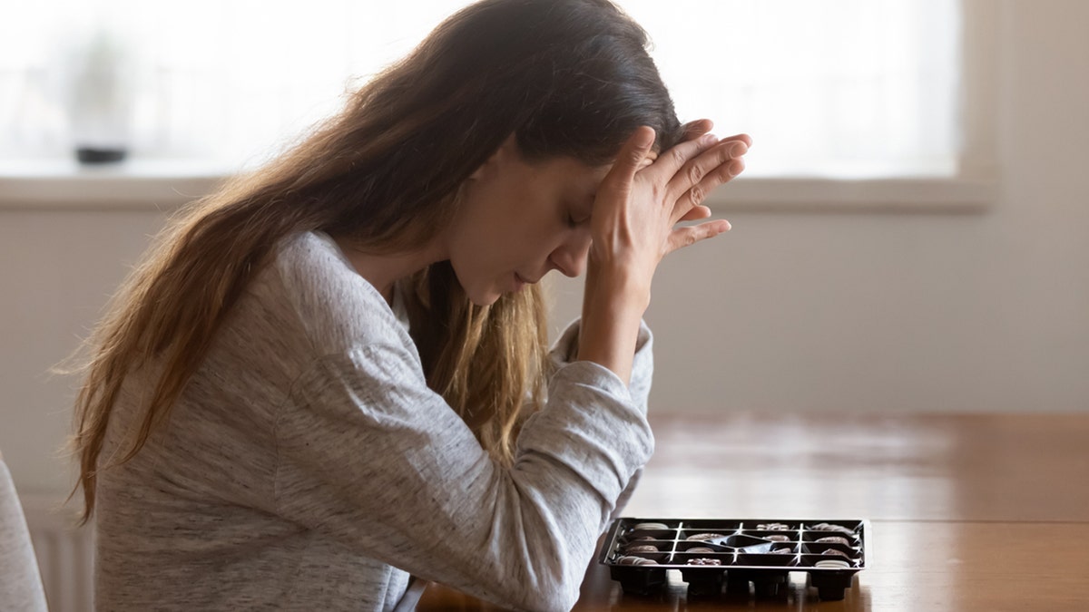 Gadis sedih duduk di meja dengan sekotak coklat