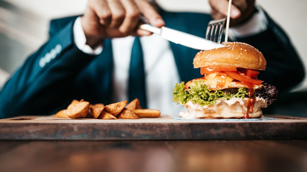 Pebisnis senior tampan duduk di restoran dan menikmati burger lezat. Konsep orang dan makanan.