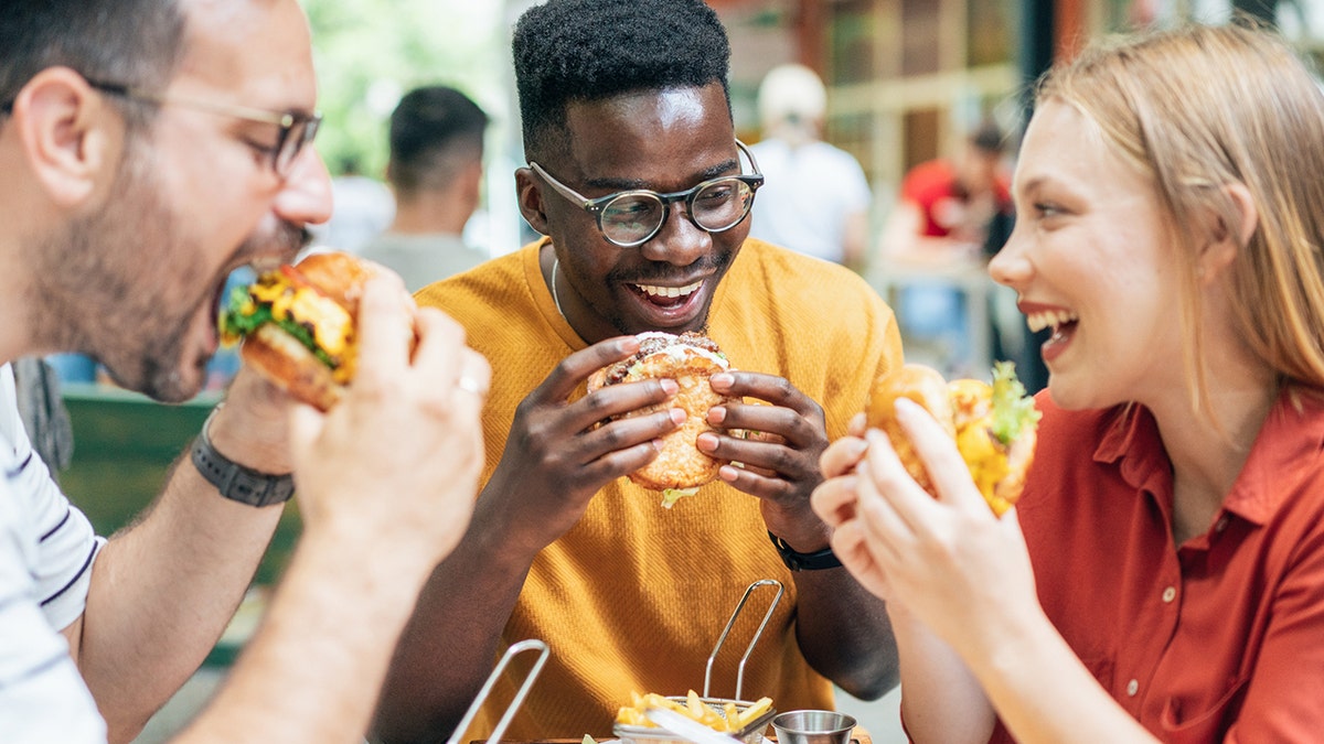 Friends eating burgers and fries at an outdoor restaurant.