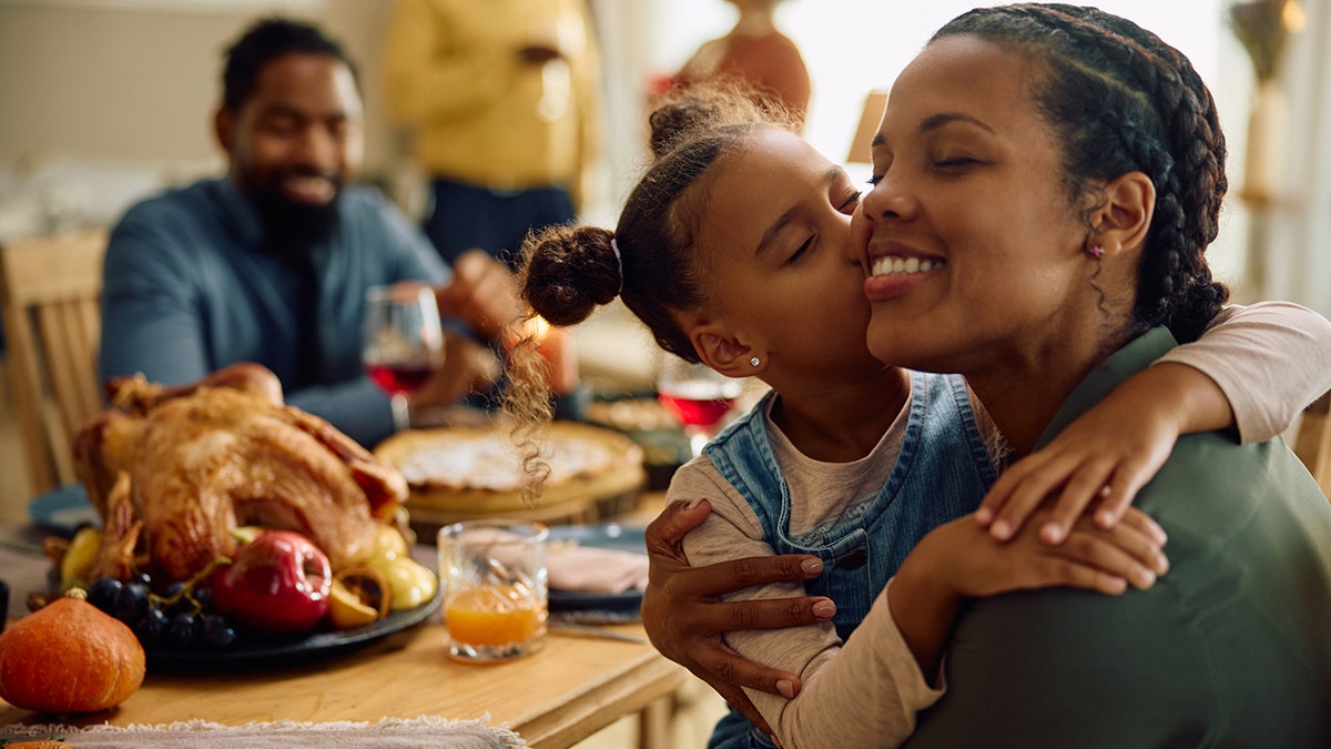 girl kissing her mother while having family dinner on Thanksgiving.