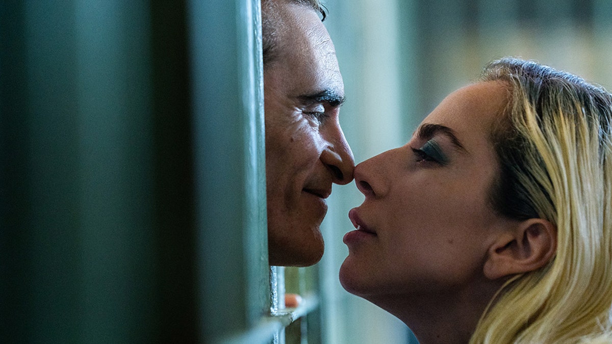 Joaquin Phoenix and Lady Gaga in character in "Joker: Folie à Deux," separated by a cell touching noses