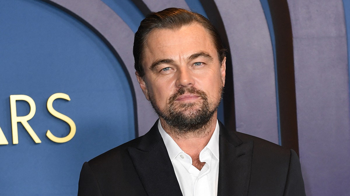 Leonardo DiCaprio in a black suit and white shirt looks serious on the carpet at the Oscars