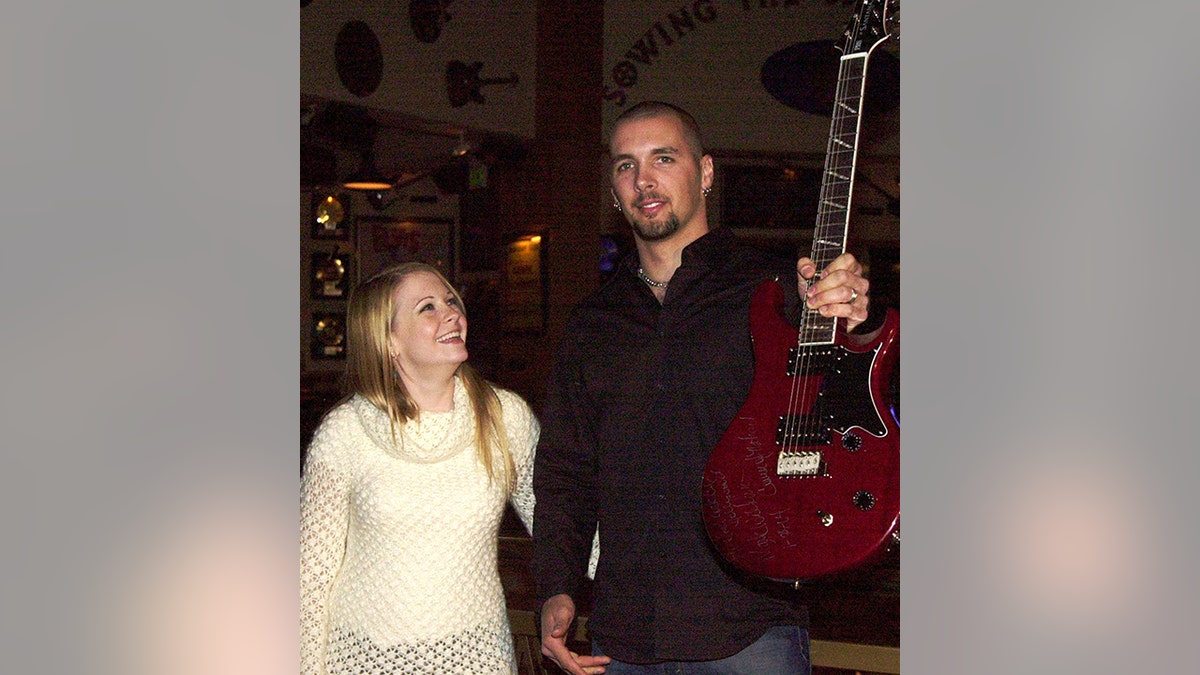 Melissa Joan Hart in a white sweater looks up at Mark Wilkerson in a black shirt holding a guitar