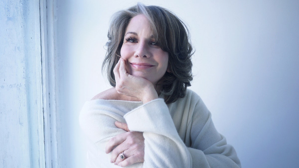 A close-up of Melissa Gilbert smiling in a white sweater.