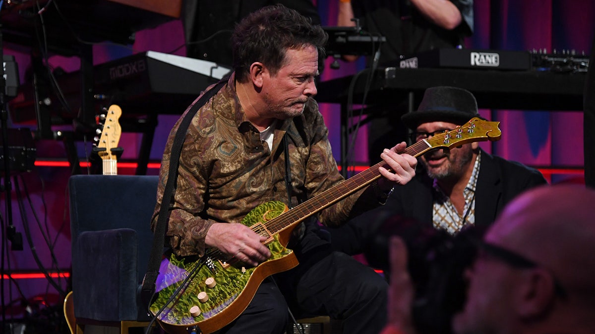 Michael J. Fox playing guitar while sitting down