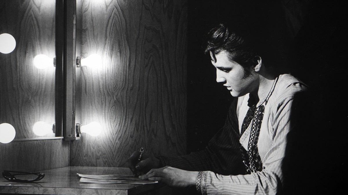 Elvis Presley looks down with the lights facing him.