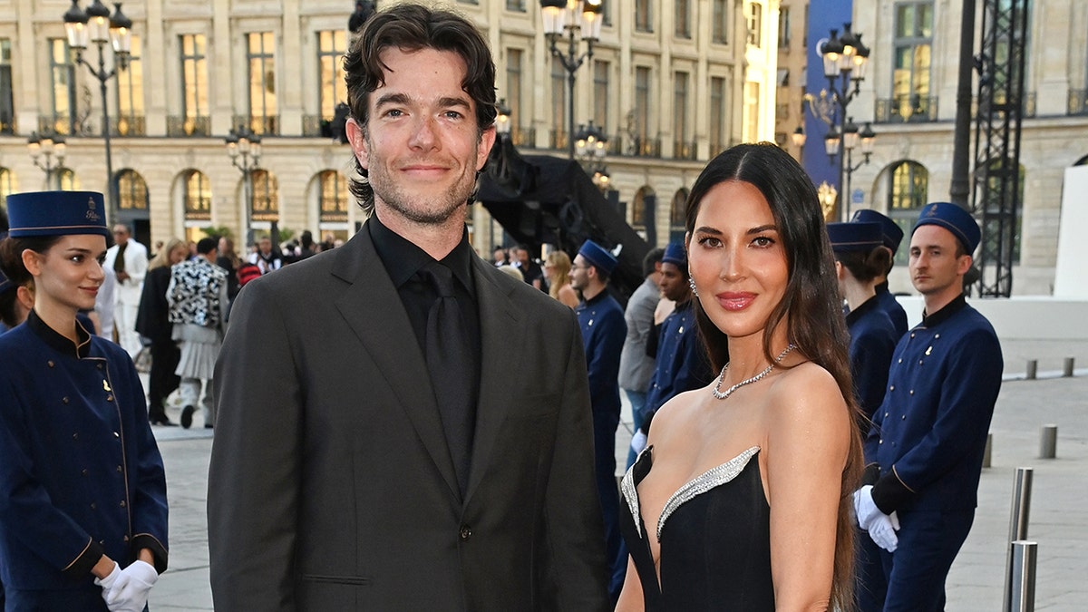 John Mulaney in a suit with Olivia Munn in a strapless pointed gown in Paris